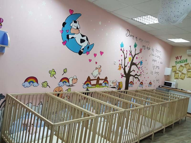 Sala de juegos con murales pintados en la pared, cunas de madera y escritorio.