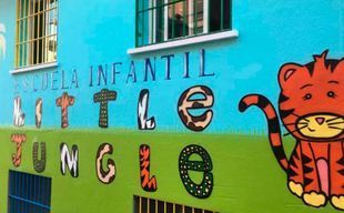 Aula preescolar colorida con mesas, sillas, estantes y decoraciones de letras en la pared.