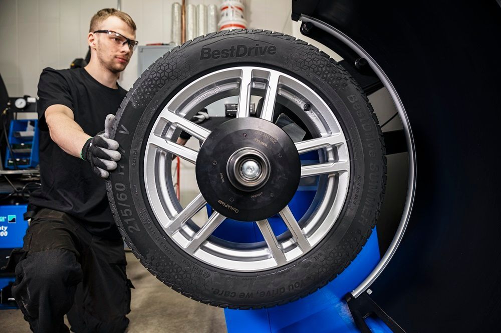 Mecánico equilibrando un neumático de automóvil con llanta plateada en una máquina en un taller.