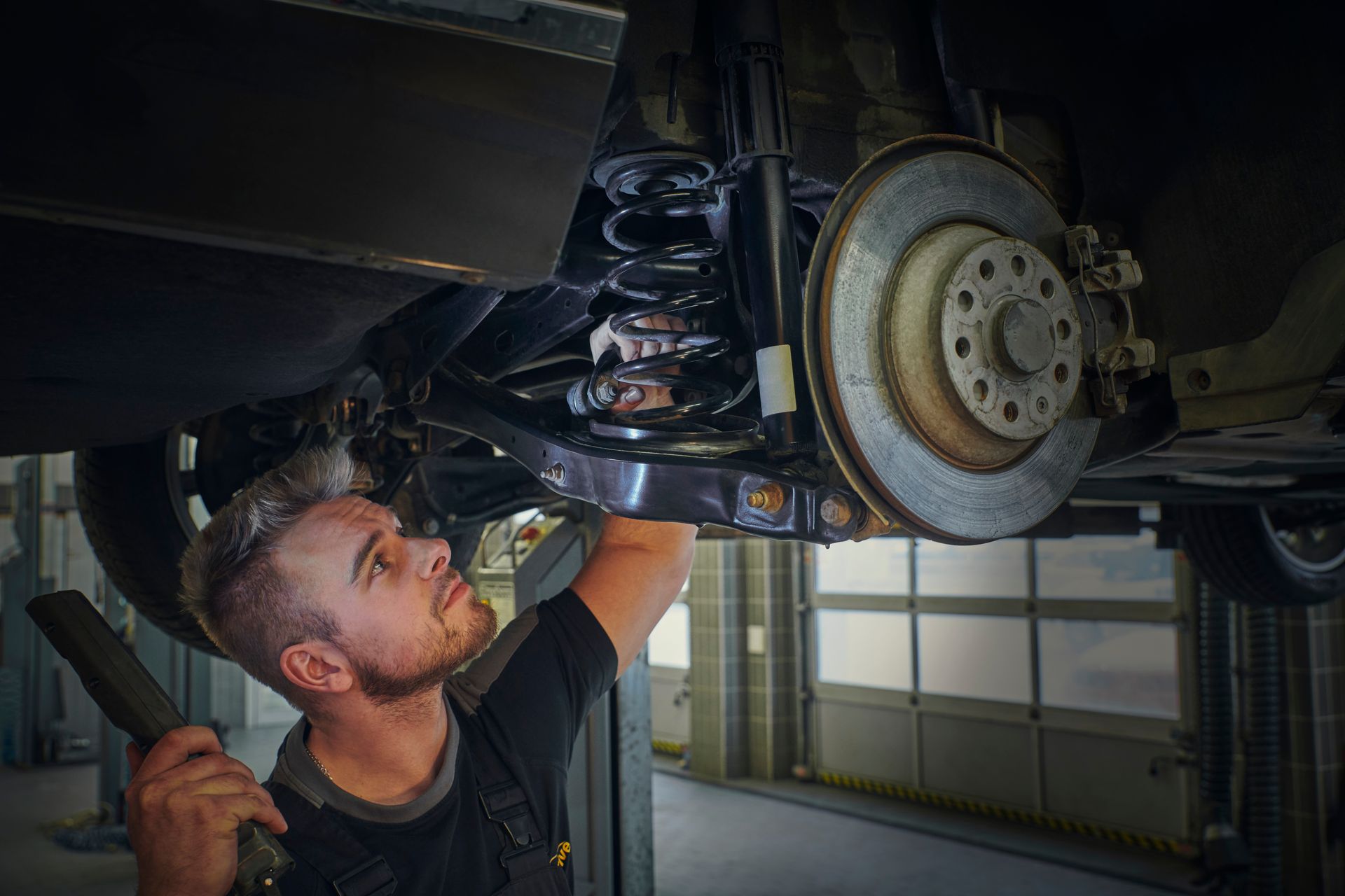 Mecánico inspeccionando la suspensión del coche, sosteniendo una herramienta en un garaje.