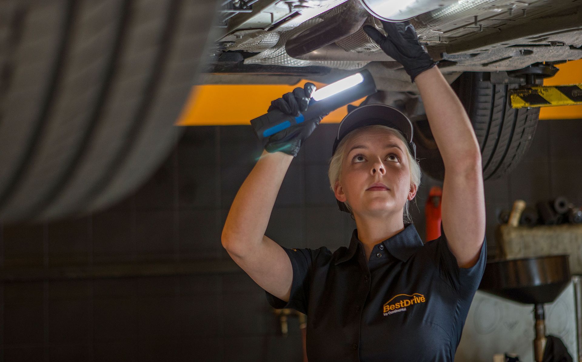 El mecánico inspecciona la parte inferior del vehículo con una linterna en un garaje.