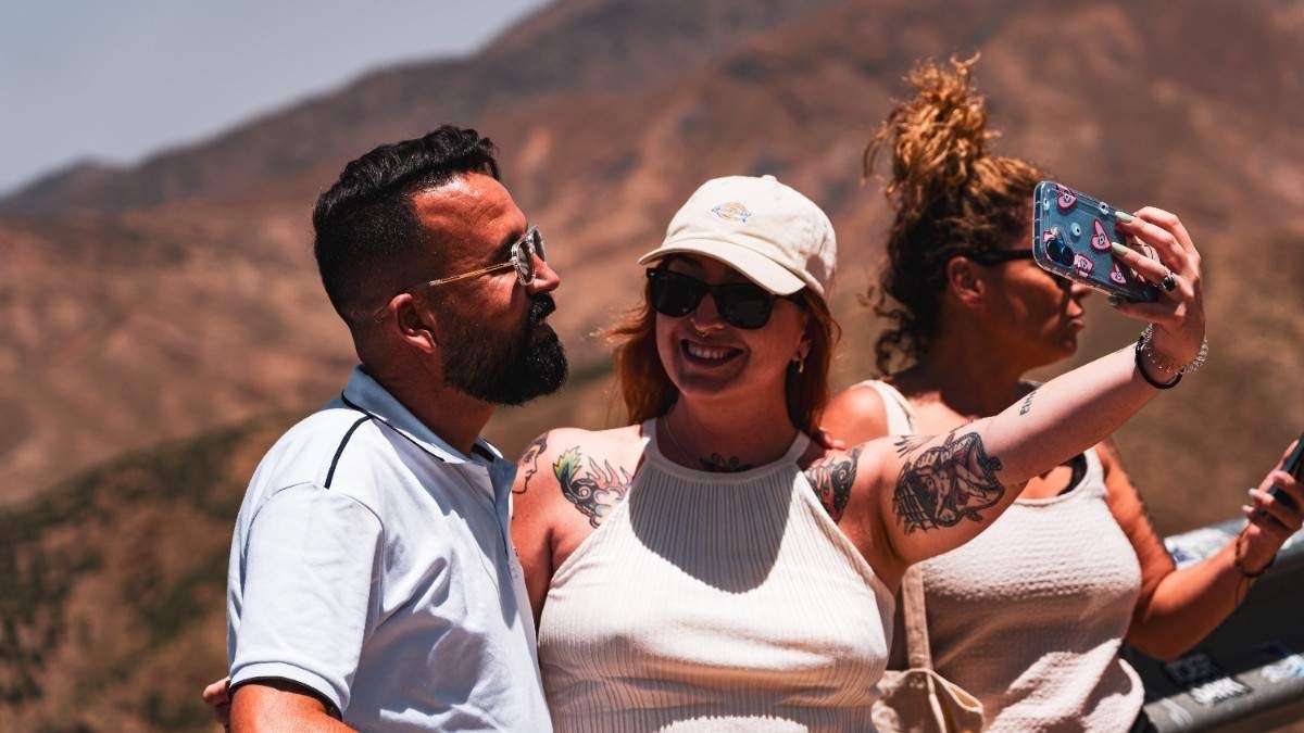 Tres personas tomándose un selfie al aire libre con montañas de fondo. Un día soleado, todos sonriendo.