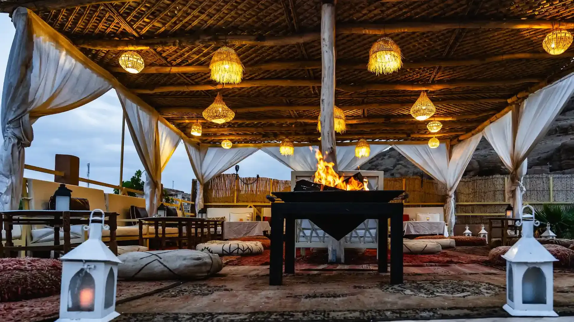 Zona de estar al aire libre con fogata, luces colgantes y linternas decorativas.