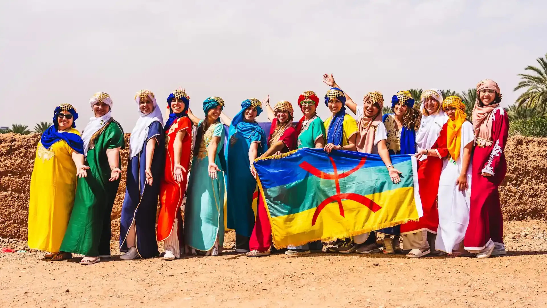 Grupo de personas con coloridas vestimentas tradicionales sosteniendo una bandera con fondo amarillo y un símbolo verde.
