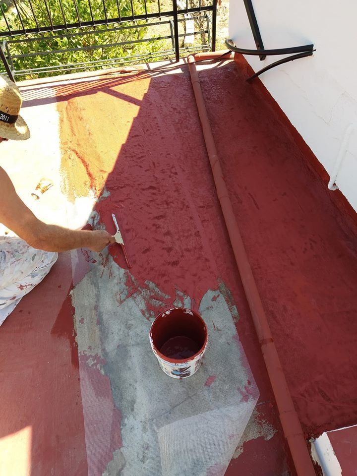 Una mujer está pintando un balcón con un balde de pintura roja.