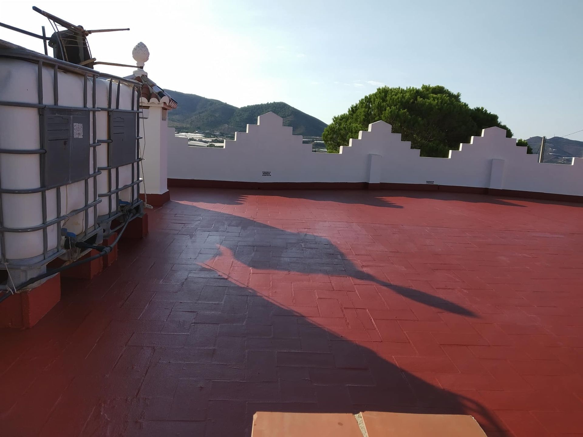 Una azotea con suelo de baldosas rojas y montañas al fondo.
