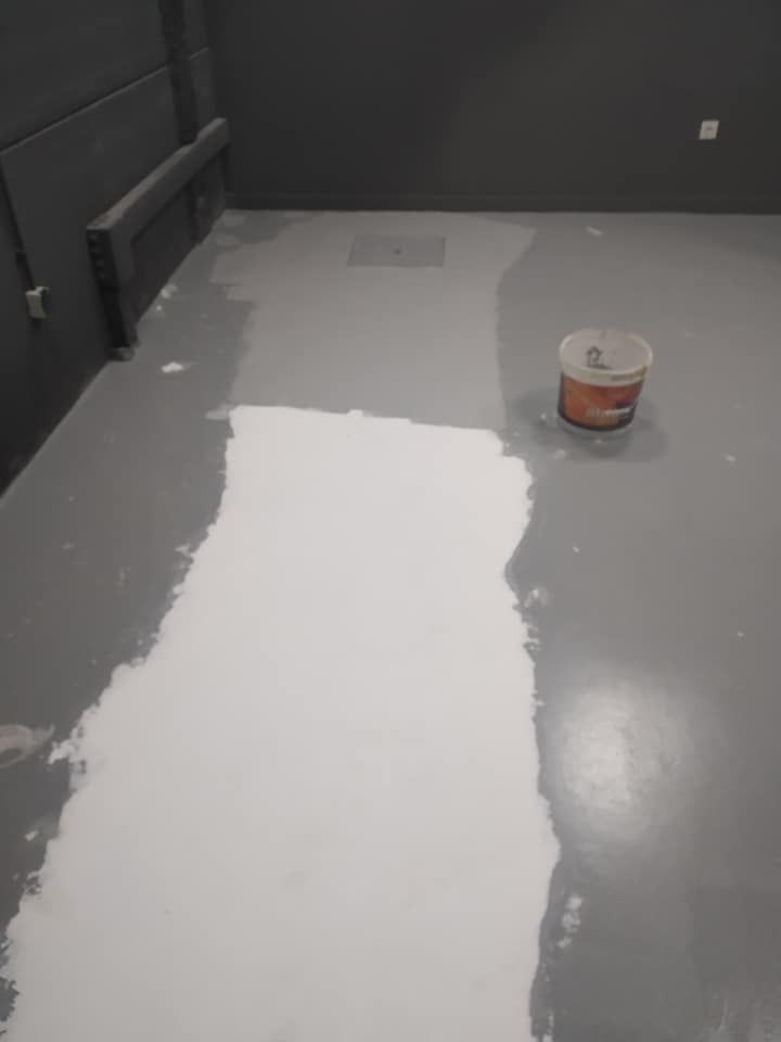 Un balde de pintura blanca reposa sobre un suelo gris.