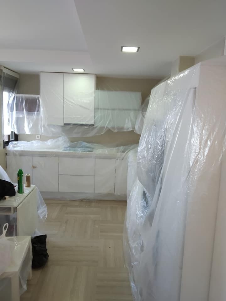 Una cocina con gabinetes blancos y un refrigerador envuelto en plástico.