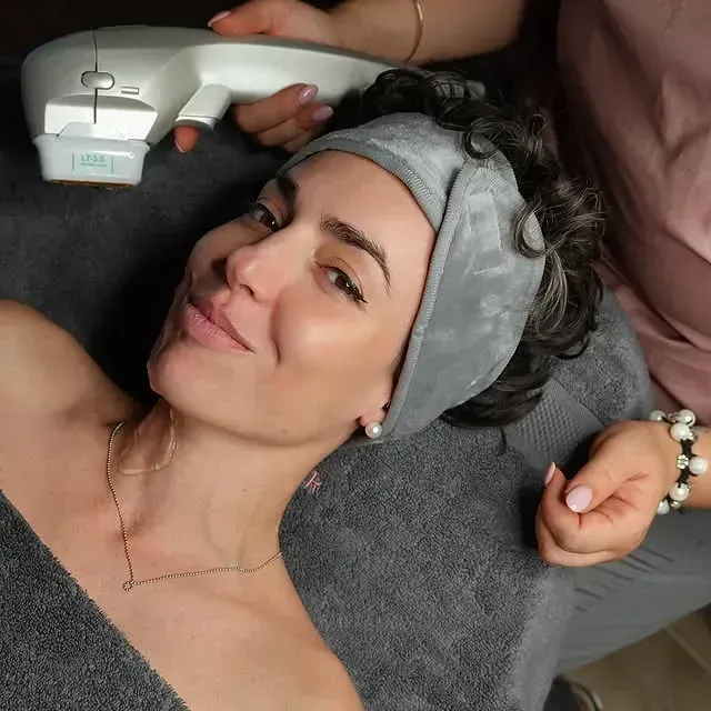 Una mujer que lleva una diadema está recibiendo un tratamiento facial.