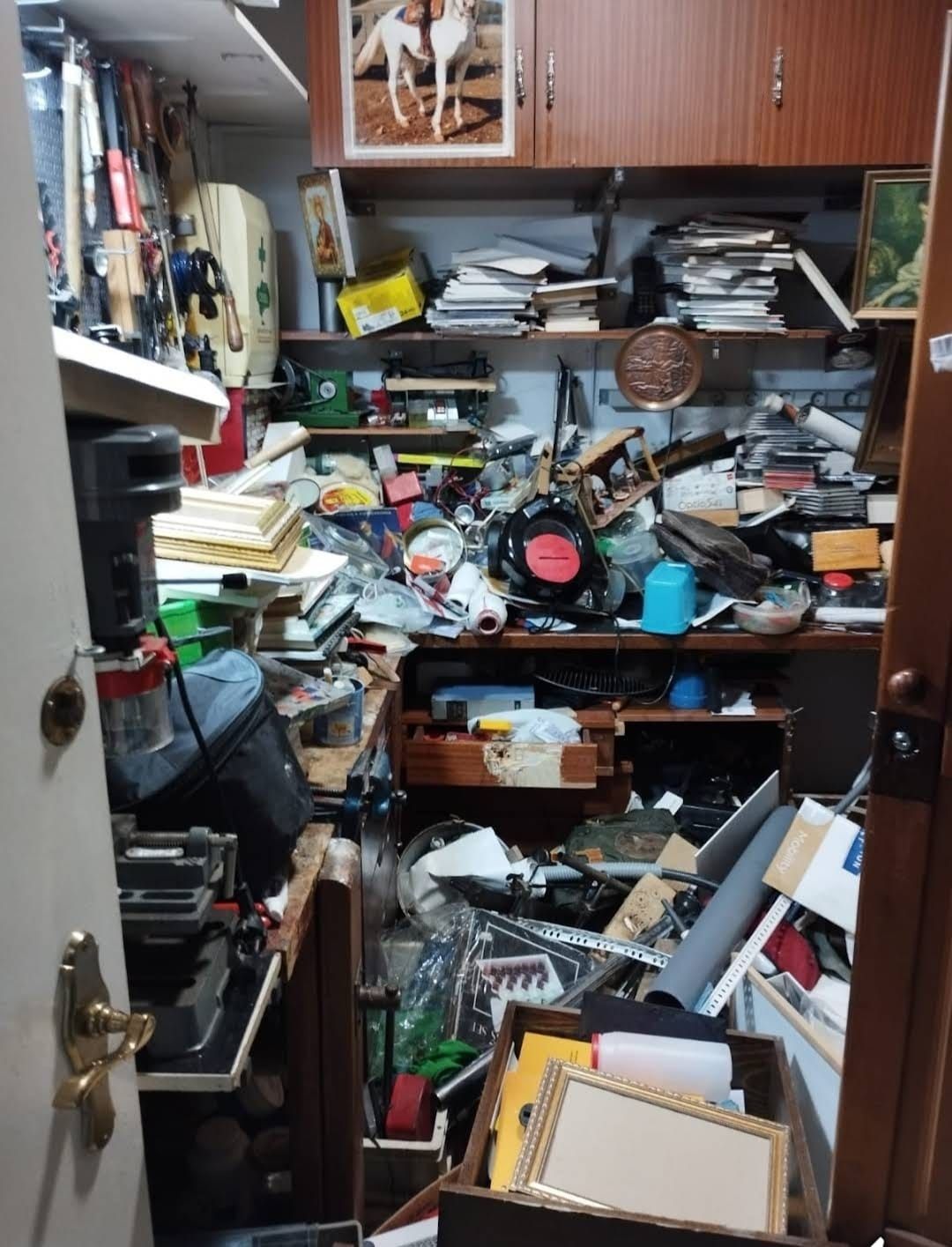 Una habitación desordenada llena de diversos objetos, incluidos papeles, cajas y herramientas; se ve un marco de puerta.