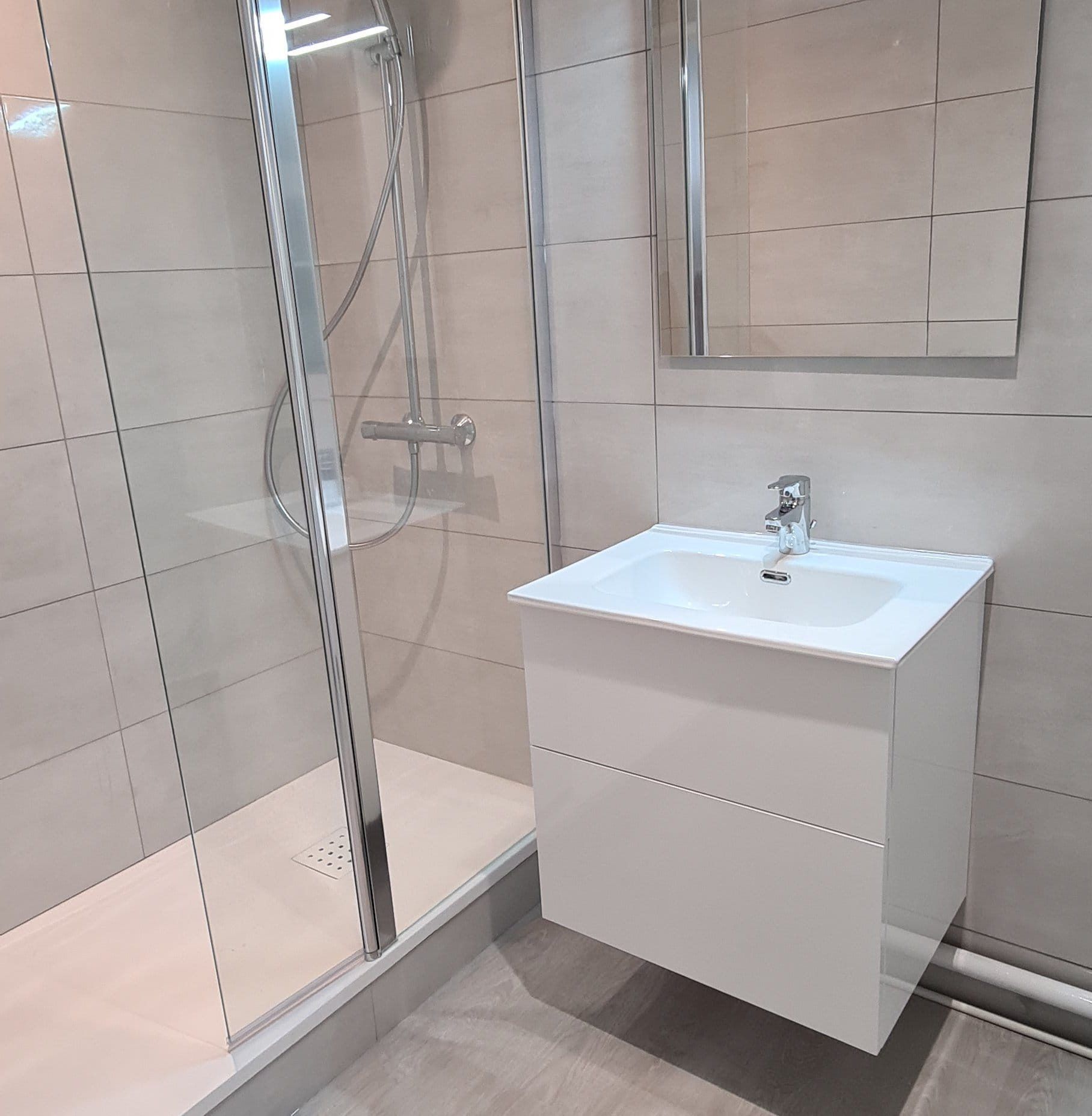 Salle de bains moderne avec douche, meuble-lavabo et miroir. Tons blancs et gris.