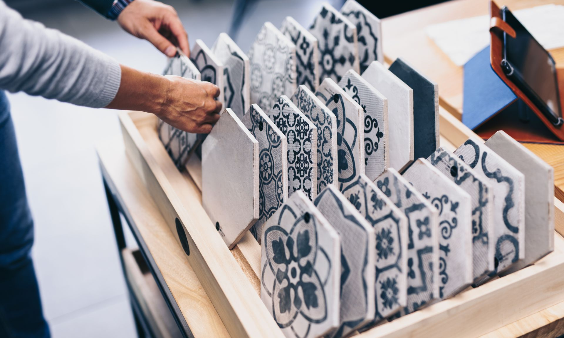 Une personne choisit des carreaux à motifs sur un présentoir en bois.