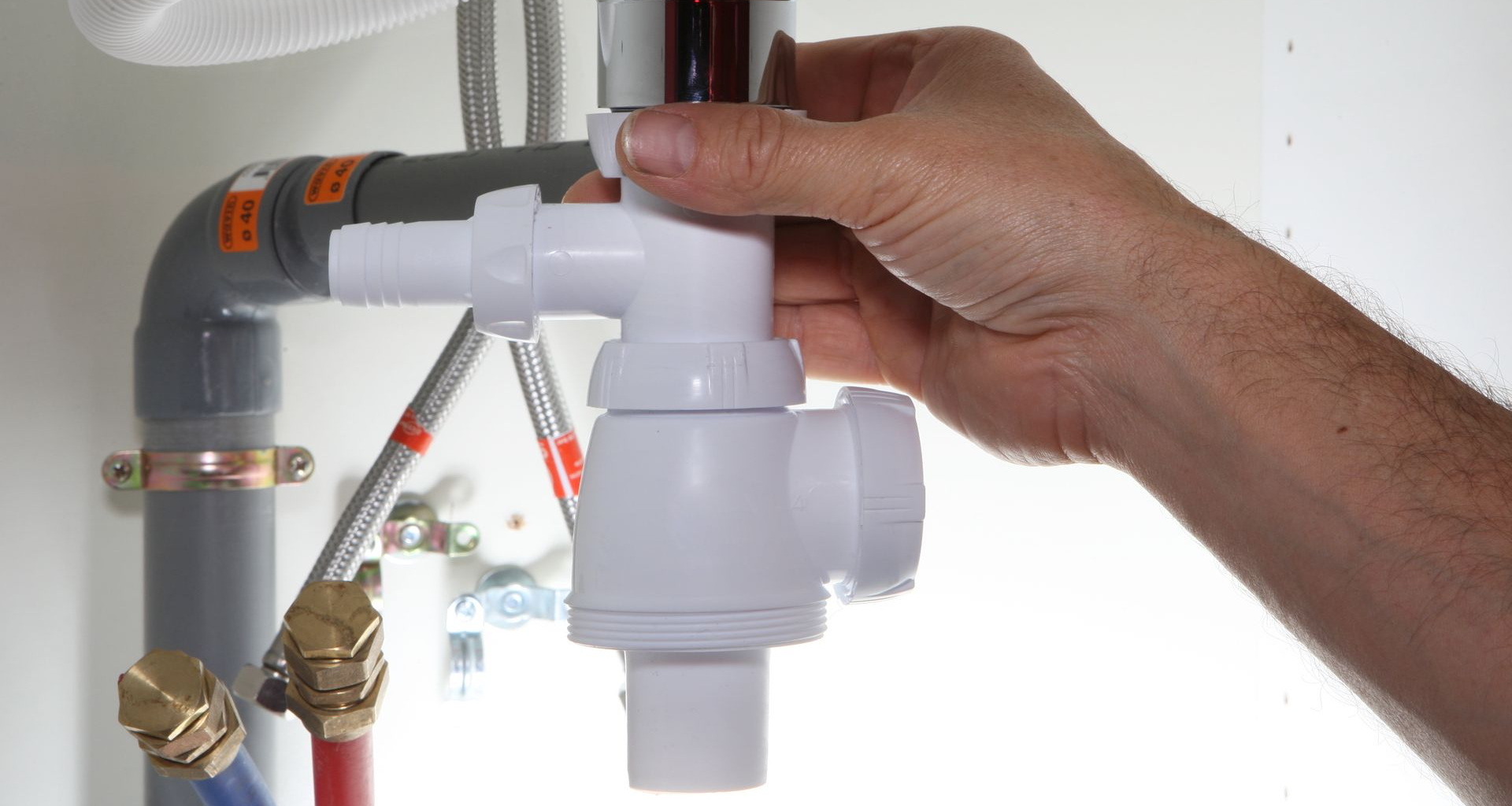 Main tenant un siphon de plomberie blanc sous un évier, en préparation de l'installation.