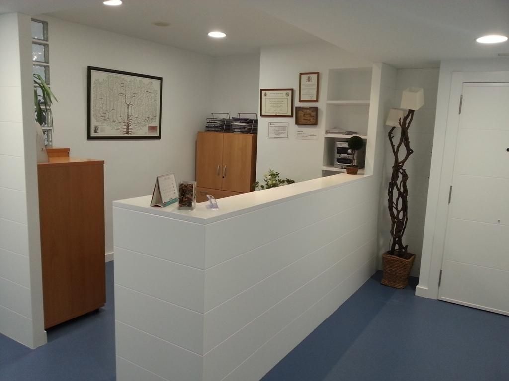 Mostrador de recepción blanco en una pequeña oficina con suelo azul claro. Un armario de madera y obras de arte en las paredes.