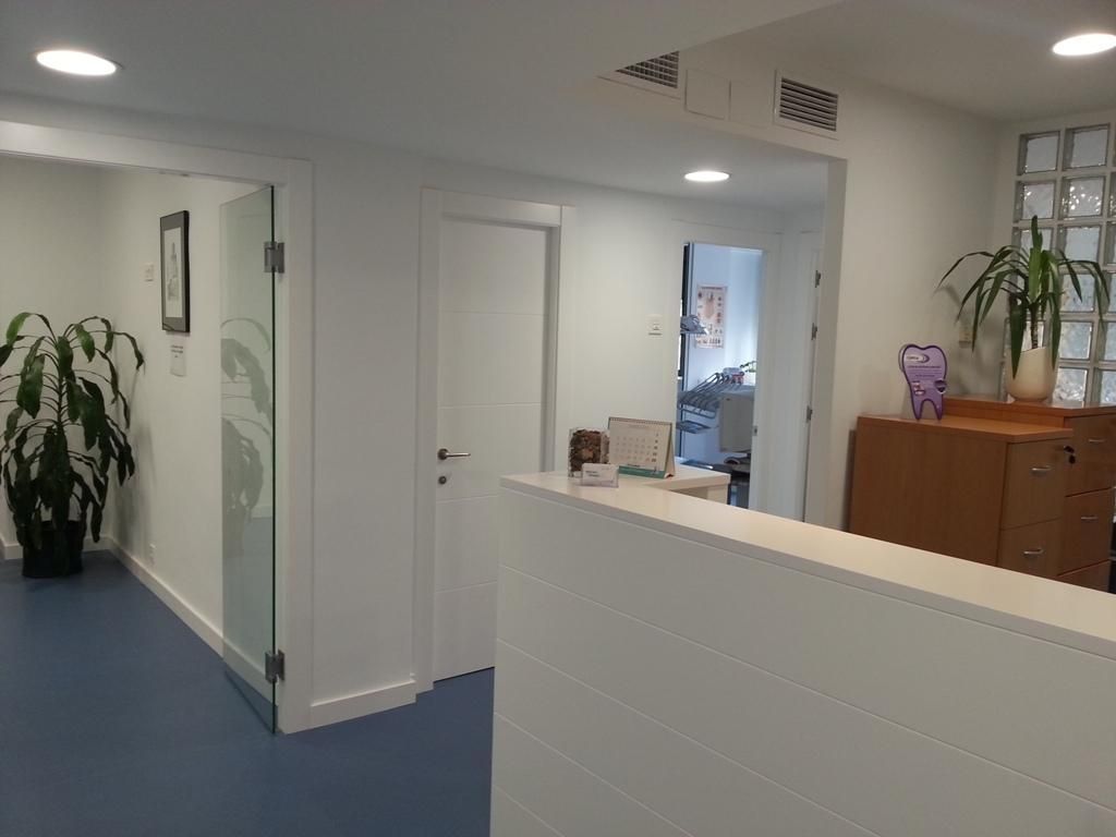 Un área de recepción de consultorio médico con un escritorio blanco, piso azul y plantas en macetas.