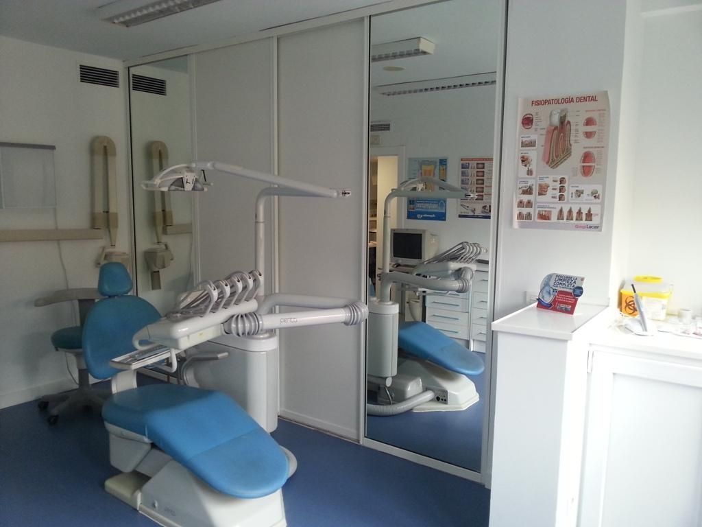 Interior de consultorio dental: Silla, equipo y espejo azules. Paredes blancas, armarios y suelo azul.