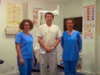 Tres profesionales médicos en un consultorio dental: un hombre con uniforme blanco y dos mujeres con uniforme azul, de pie y sonriendo.