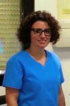 Una mujer con uniforme azul y gafas sonríe en un entorno de oficina.