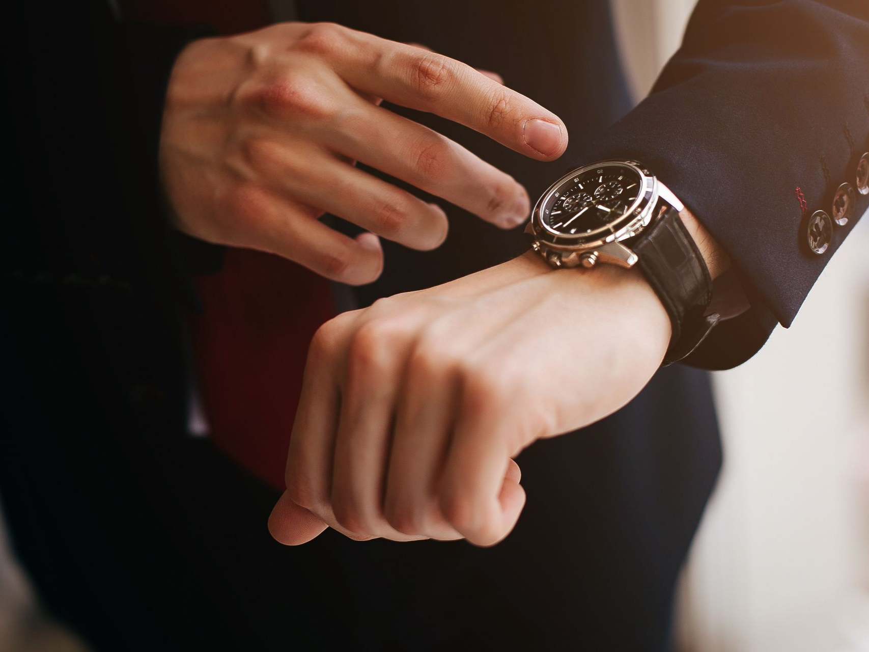 Personne en costume regardant une montre-bracelet, soulignant l'importance du temps.