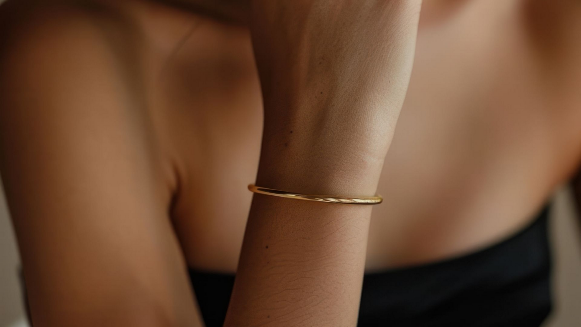 Bras de femme avec un fin bracelet en or, fond flou.