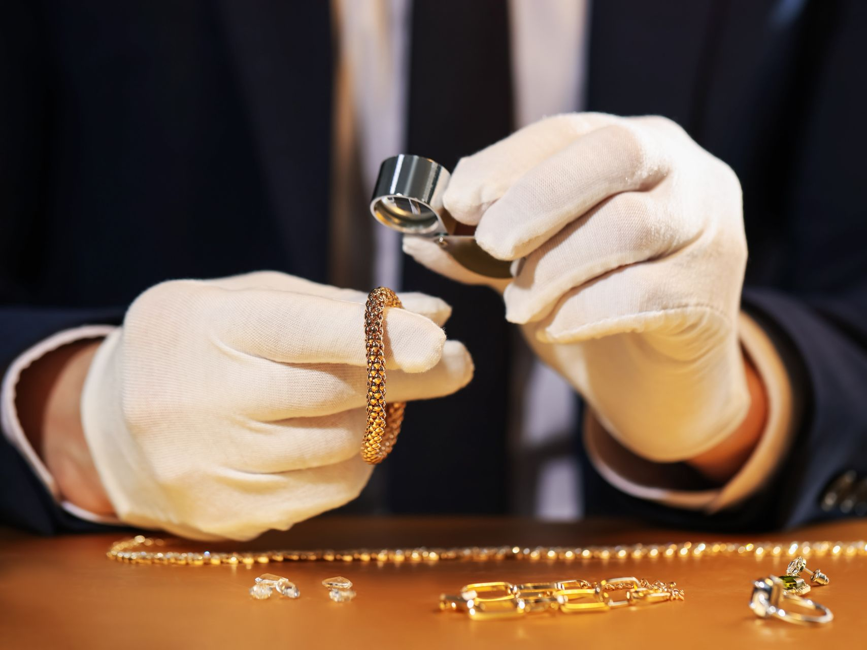 Une personne portant des gants blancs examine des bijoux en or avec une loupe.