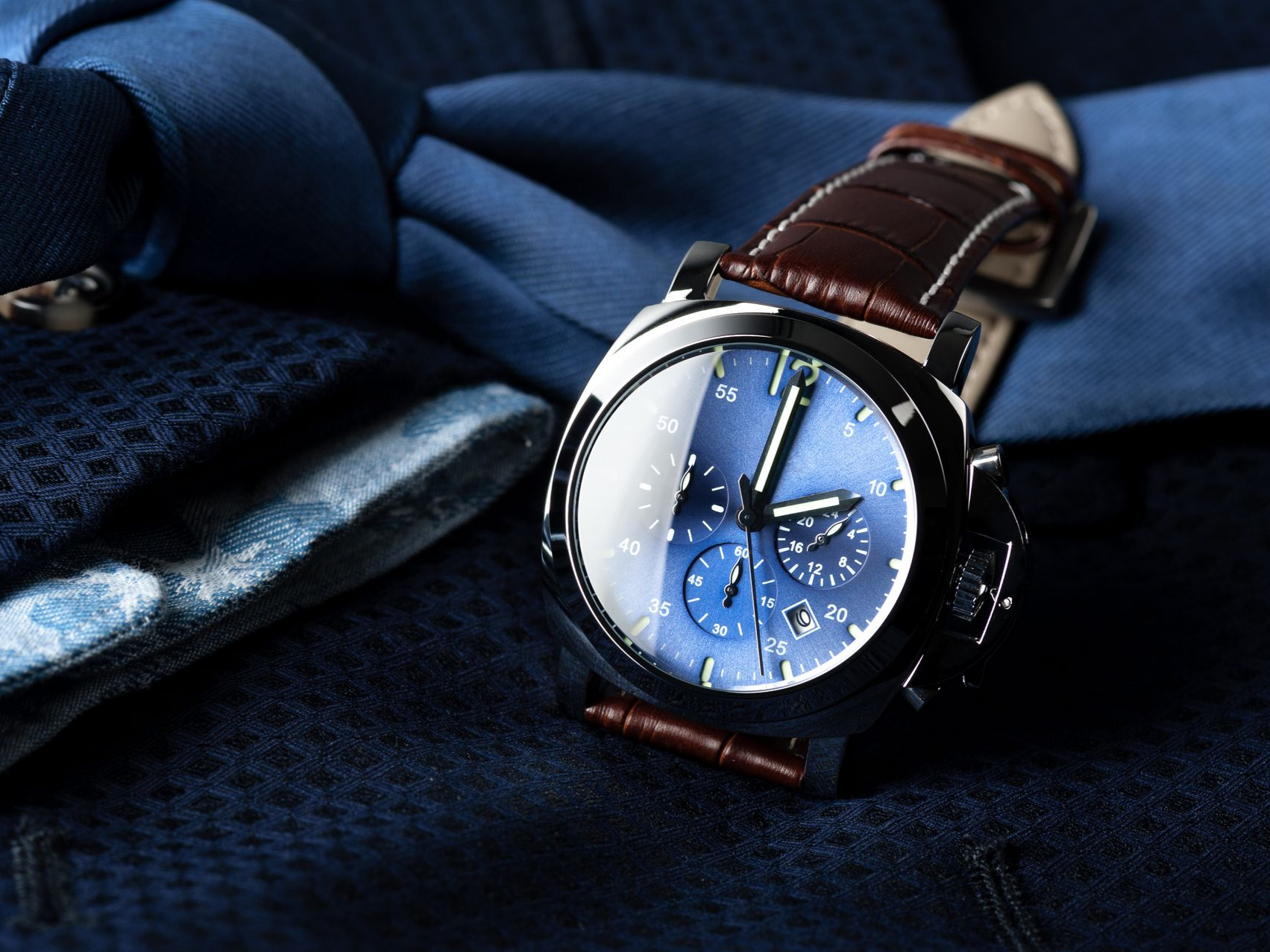 Montre-bracelet à cadran bleu avec bracelet en cuir marron, montée sur un costume bleu avec une cravate en soie.