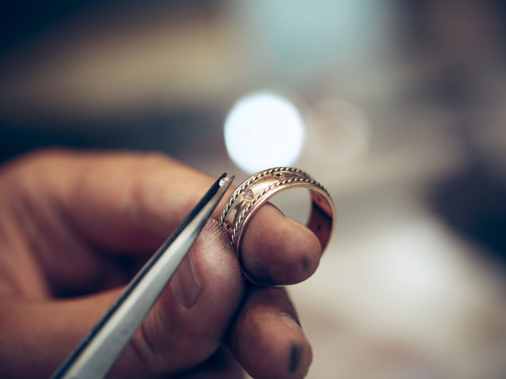 Main tenant une bague en or avec une pince, se préparant à la réparer ou à l'ajuster.