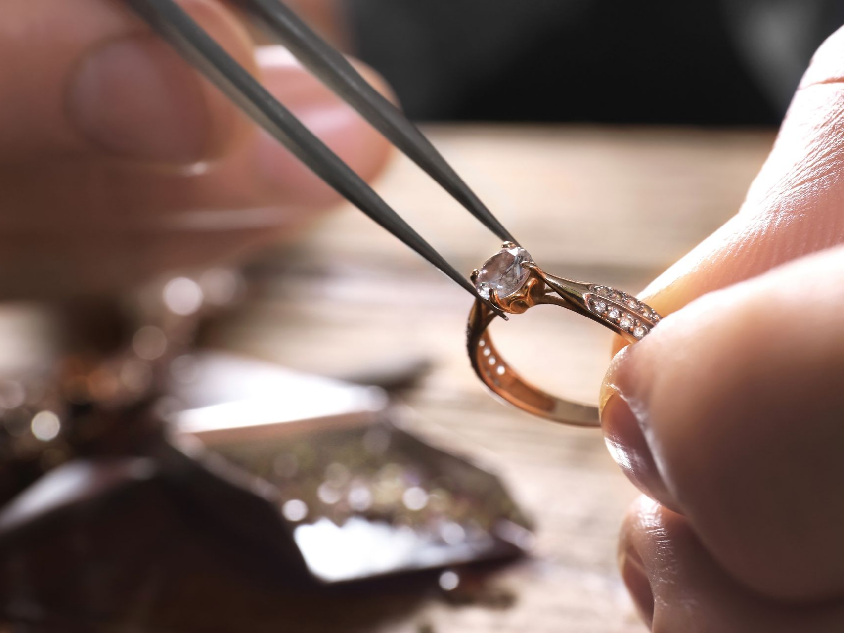 Une main utilisant une pince très fine pour sertir un diamant dans une bague en or, gros plan.