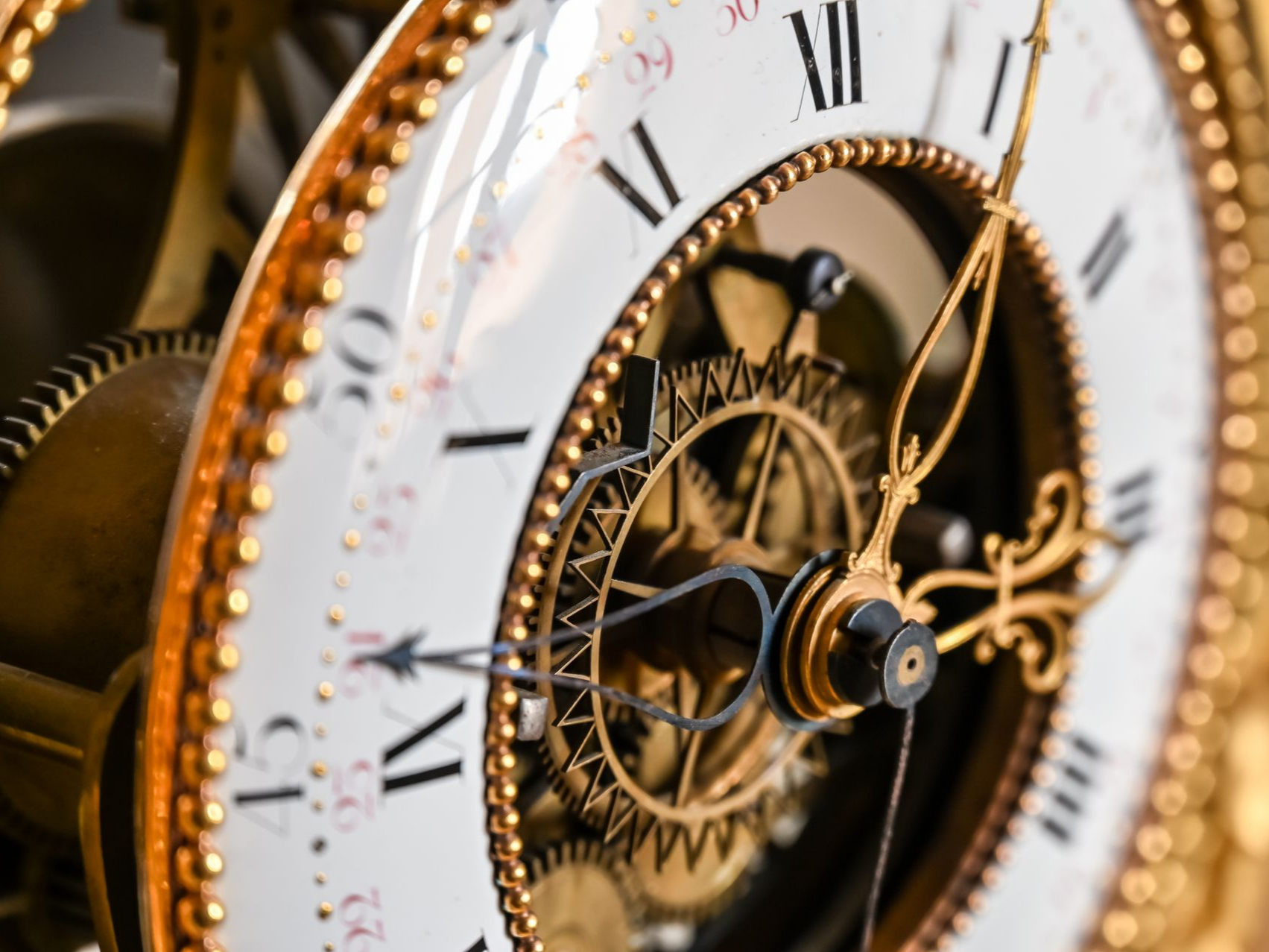 Gros plan sur un cadran d'horloge antique en or avec chiffres romains et engrenages internes visibles.