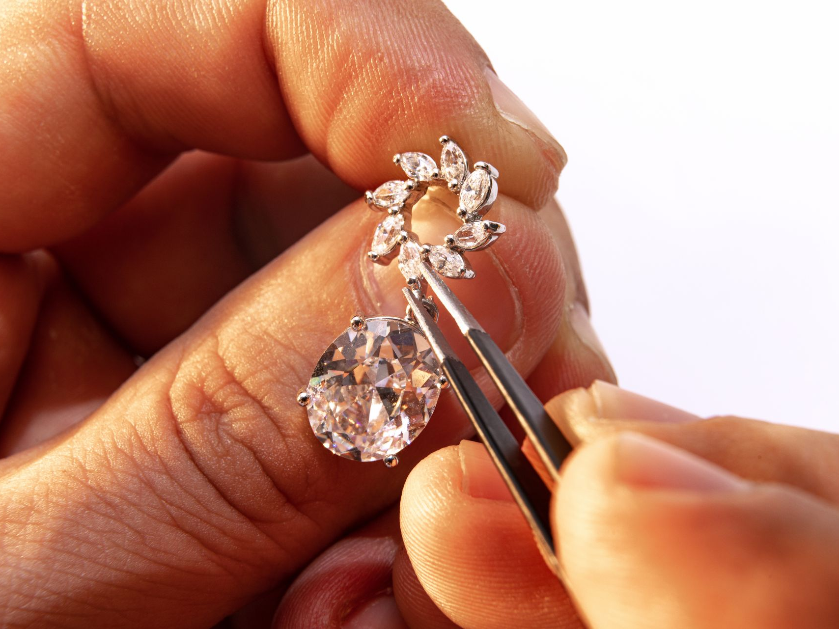 Mains tenant une boucle d'oreille en diamant avec une pince sur un fond blanc.