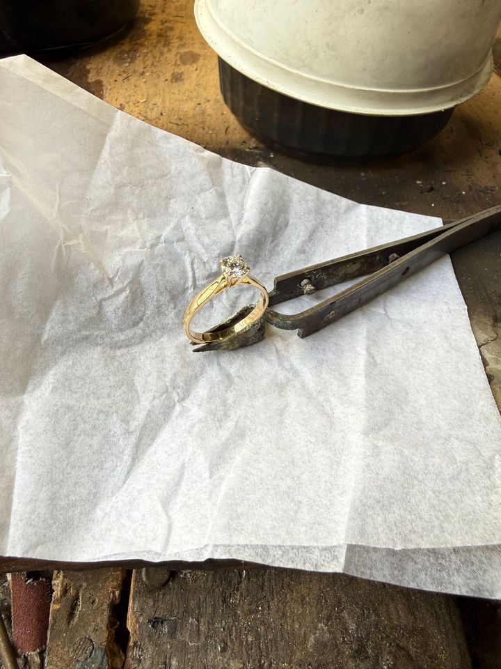 Une main utilisant une pince très fine pour sertir un diamant dans une bague en or, gros plan.