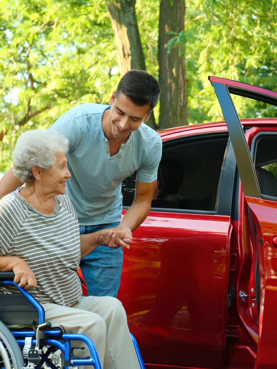 Un homme aide une personne en fauteuil roulant à monter dans une voiture rouge.