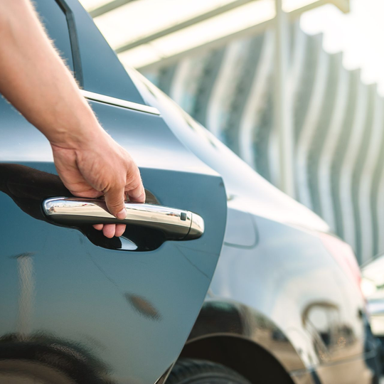 Une main ouvre une portière de voiture noire et brillante ; journée ensoleillée.