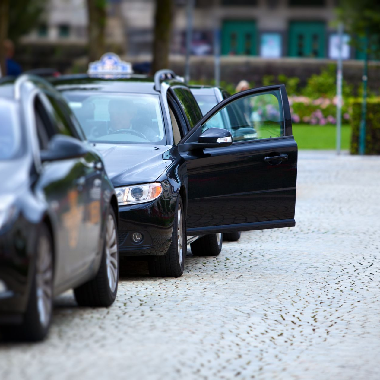 Un taxi noir, portière ouverte, est stationné dans une rue pavée, en attente d'un passager.