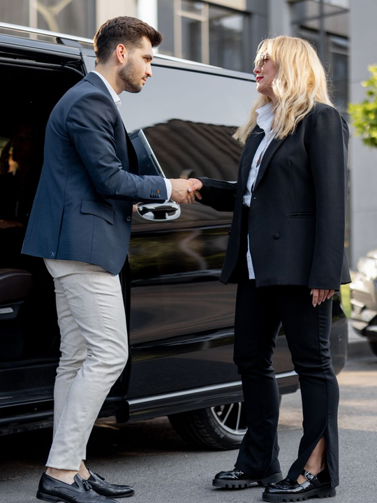 Un homme et une femme se serrent la main près d'une voiture noire. Ils sont tous deux en tenue de travail, à l'extérieur.