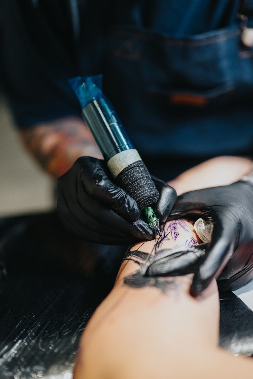 Brazo de una persona recibiendo un tatuaje; artista con guantes negros, utilizando una máquina de tatuar.