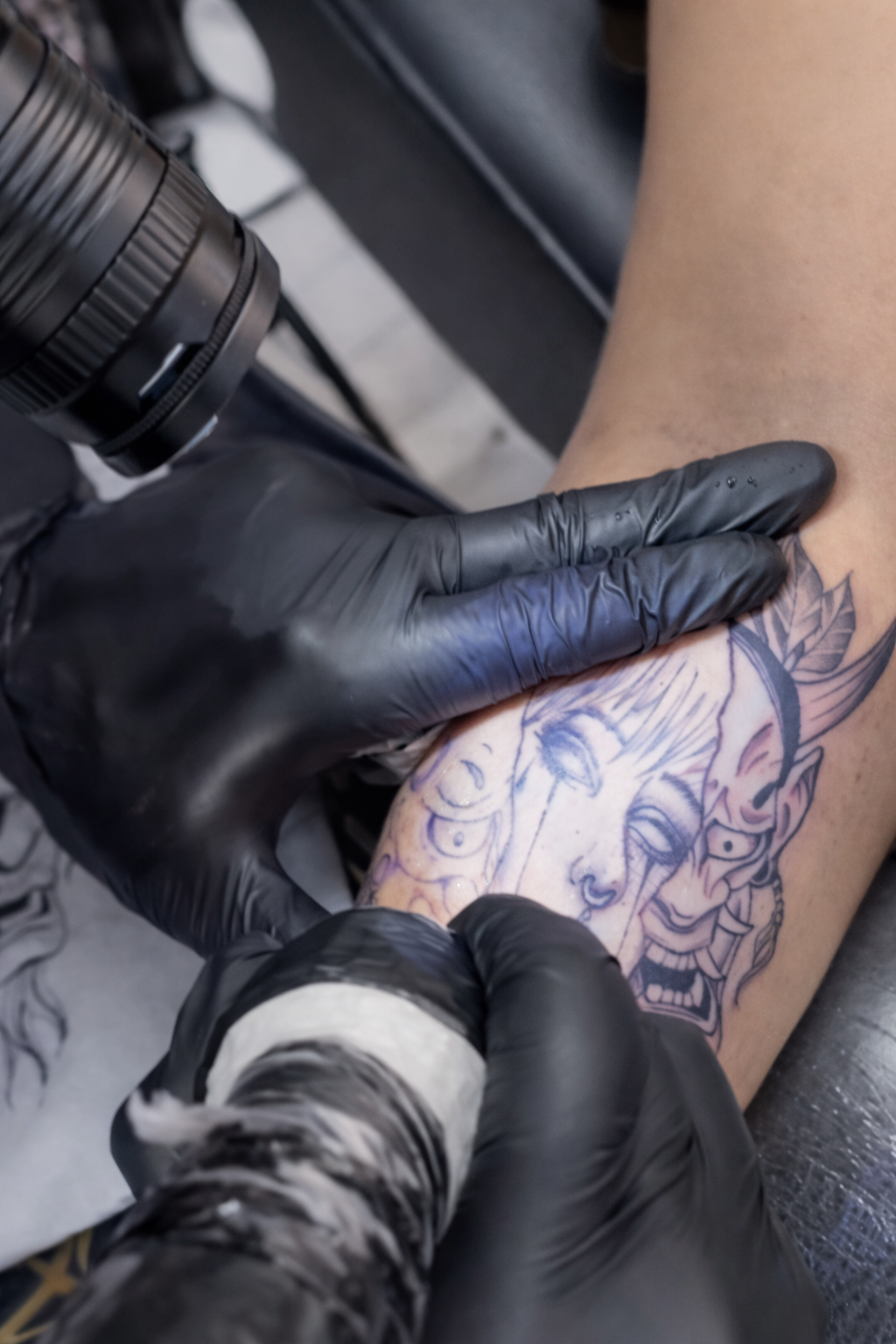 Artista del tatuaje con guantes negros, utilizando una máquina de tatuar en el brazo de una persona.