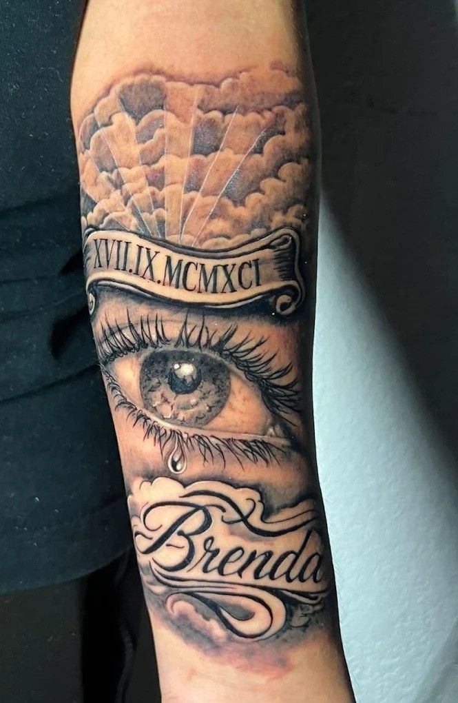 Tatuaje de un ojo llorando bajo un cielo nublado con el nombre