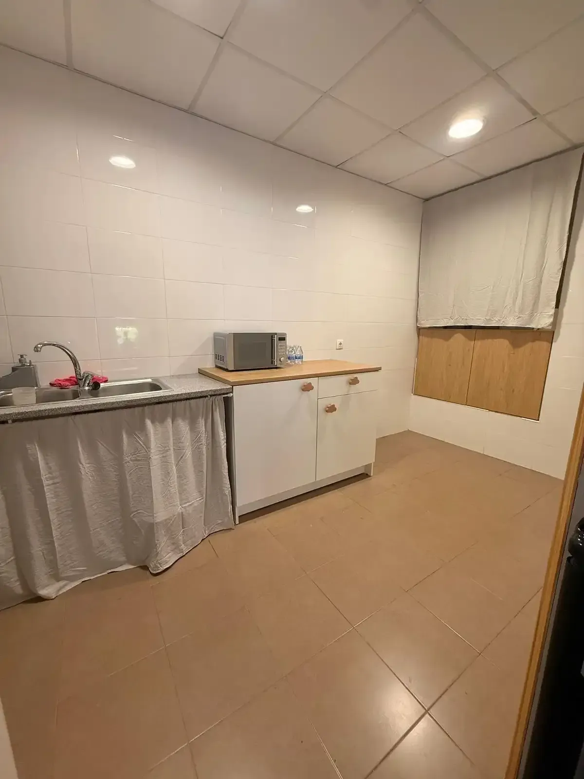 Pequeña zona de cocina con armarios blancos, microondas, fregadero
