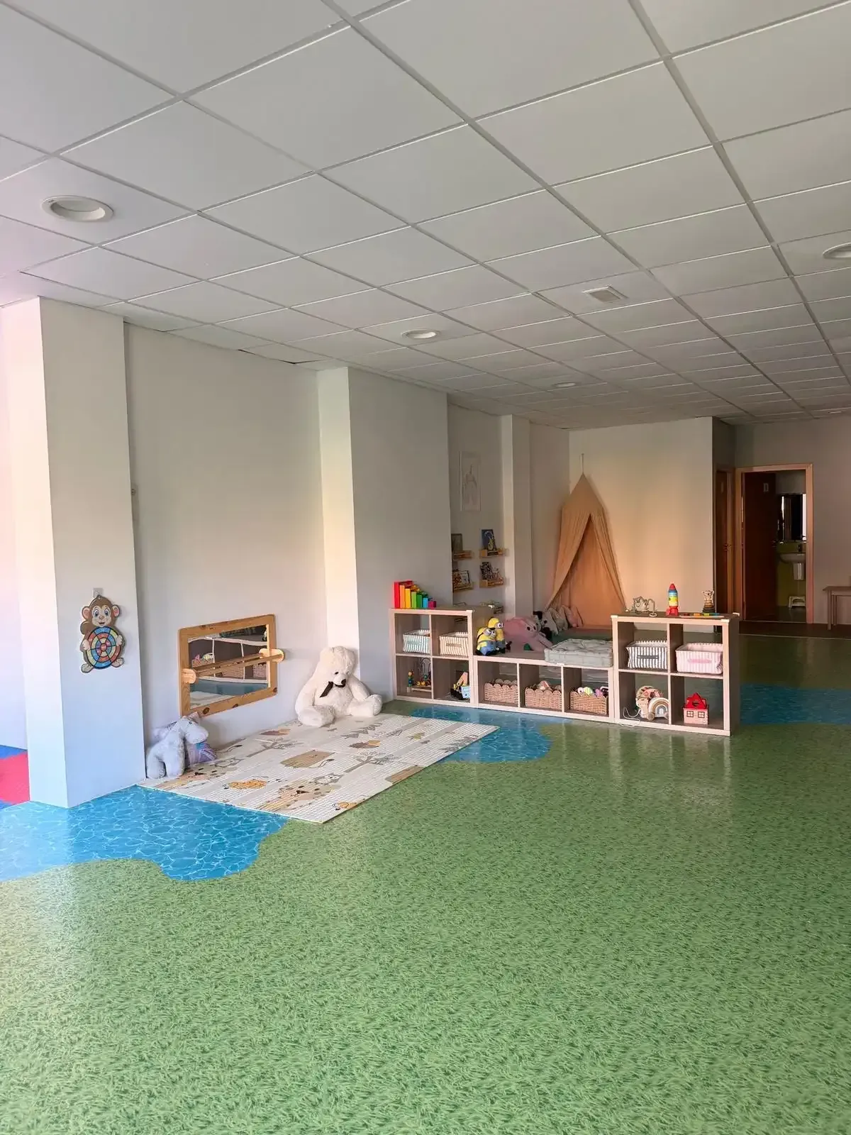 Sala de juegos con suelo verde, paredes blancas, juguetes