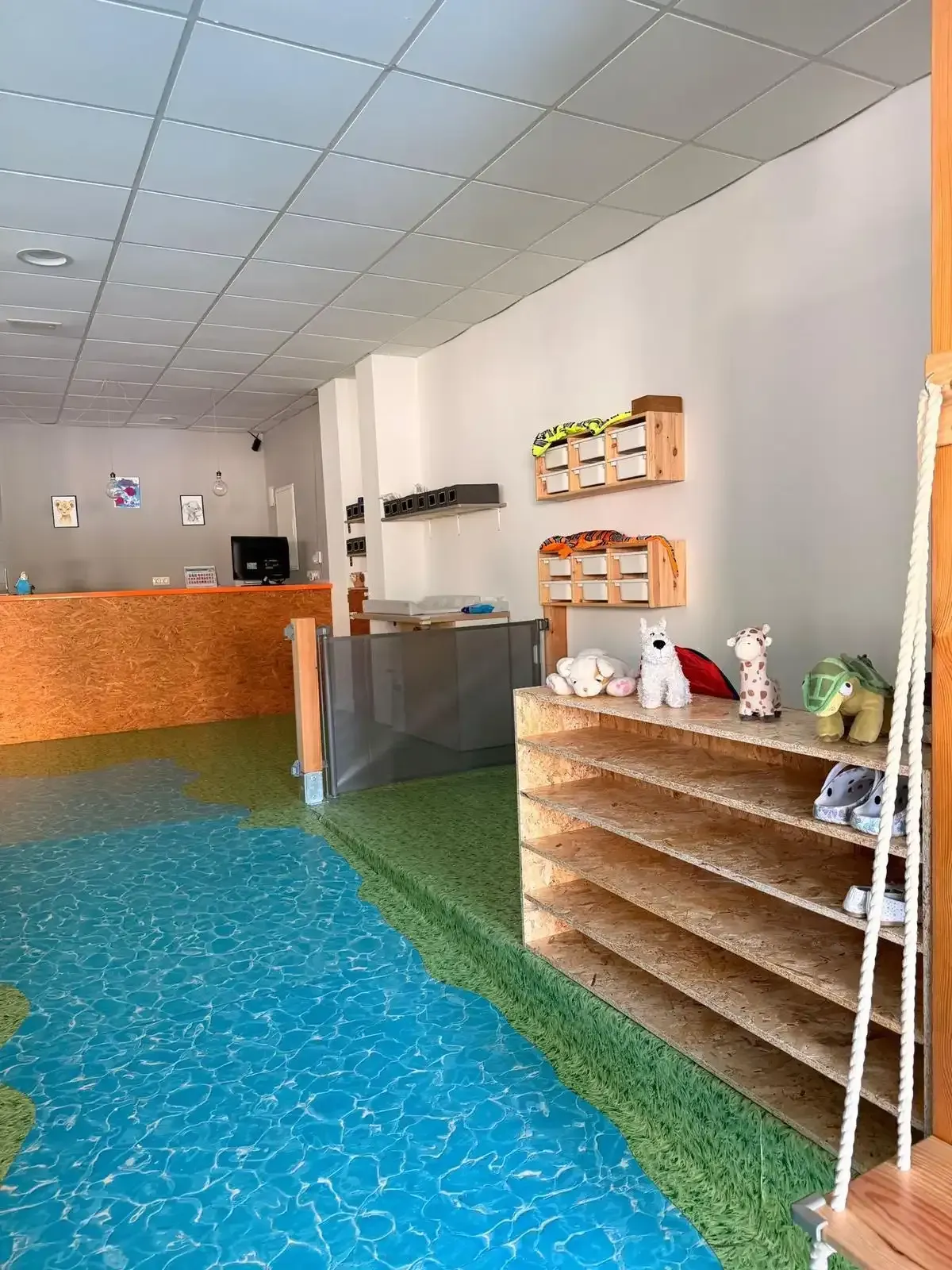 Zona de piscina interior vacía con suelo turquesa, techo de azulejos, mostrador de recepción y estanterías en la pared.