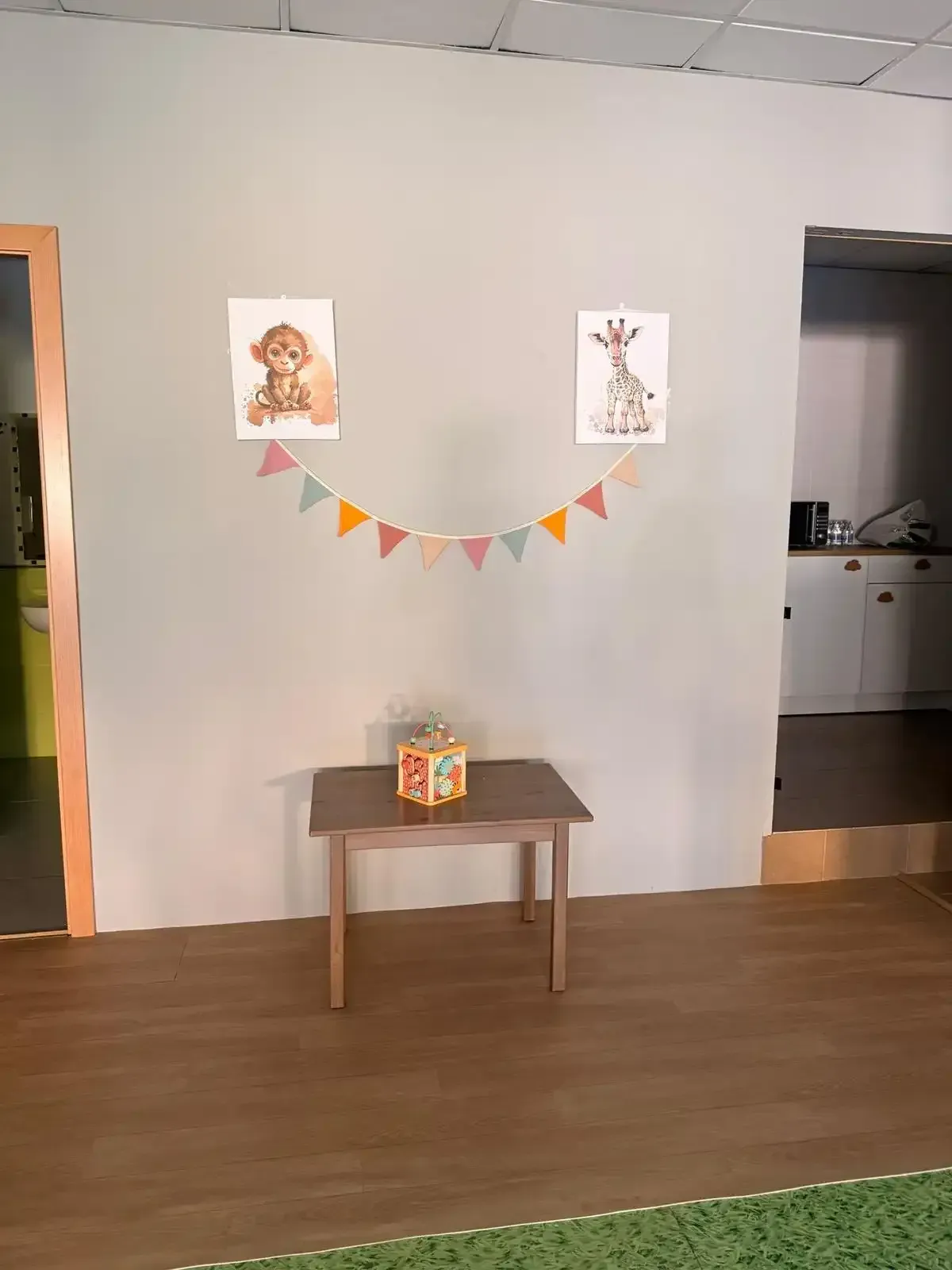Mesita con una caja de regalo debajo de una pancarta colorida entre dos láminas enmarcadas en una habitación.