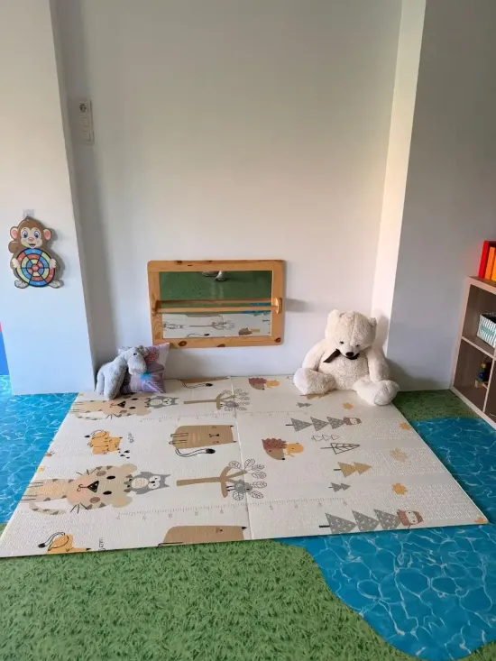 Un rincón de juegos colorido con colchonetas de espuma, un perro de peluche blanco y una pequeña pizarra en la pared.
