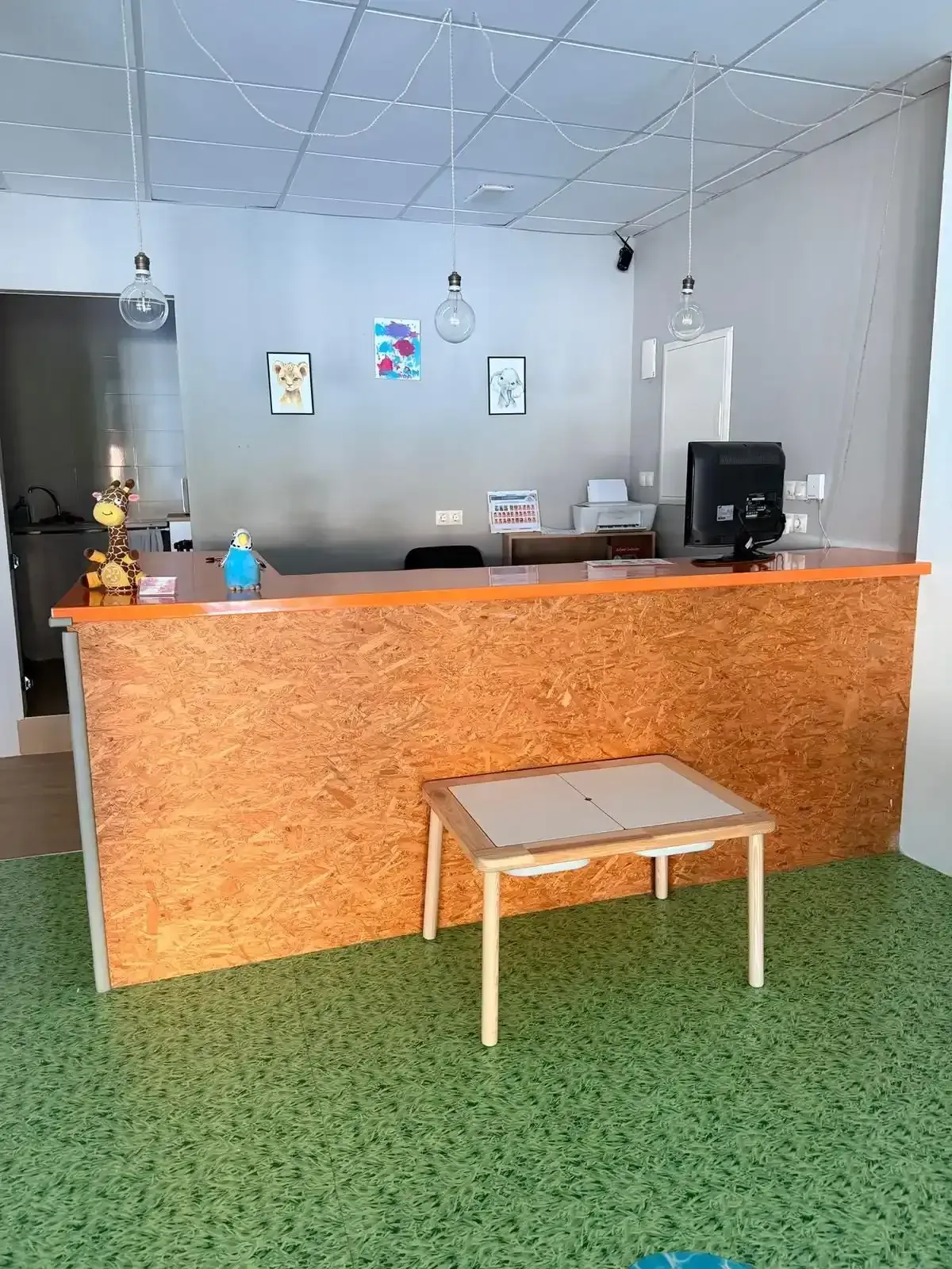 Mostrador de recepción de oficina pequeño con frontal de madera naranja, banco y alfombra verde.