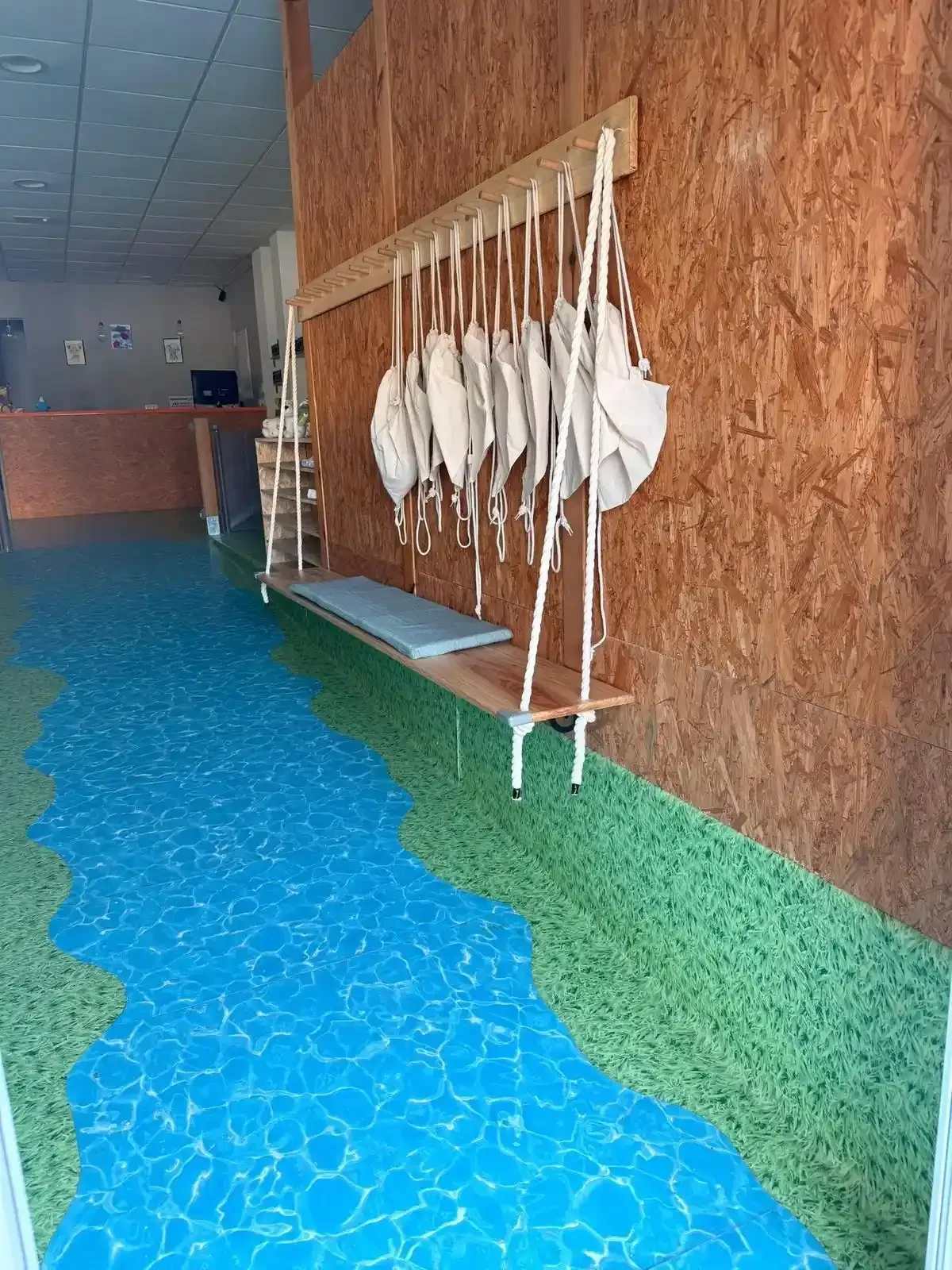 Pasillo con suelo moteado de azul y verde, pared revestida de madera y adornos colgantes de tela blanca.