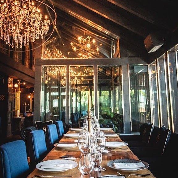 Comedor formal con mesa larga preparada para comer, sillas azules, lámpara de araña y pared con espejos.