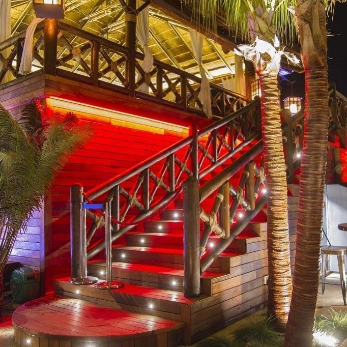 Escalera de madera con iluminación roja, que conduce a una estructura con barandilla decorativa y luces exteriores.
