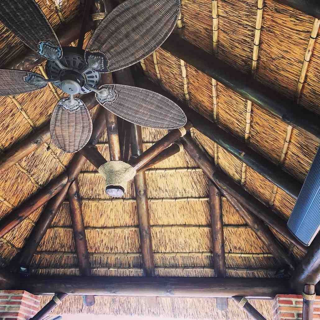 Ventilador de techo de mimbre bajo una estructura de techo de paja con vigas de madera.
