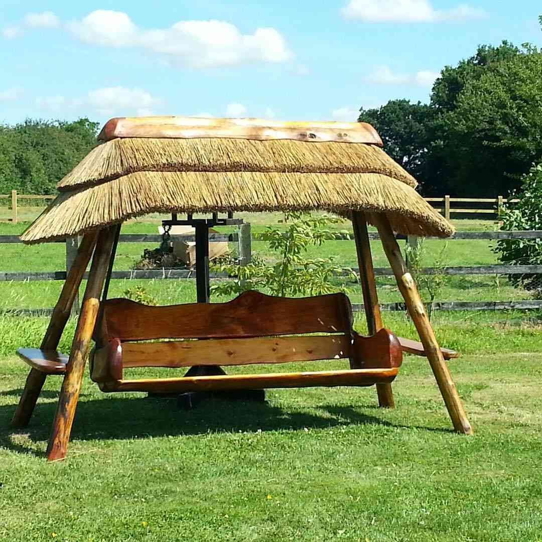 Columpio de madera con techo de paja en un patio con césped.