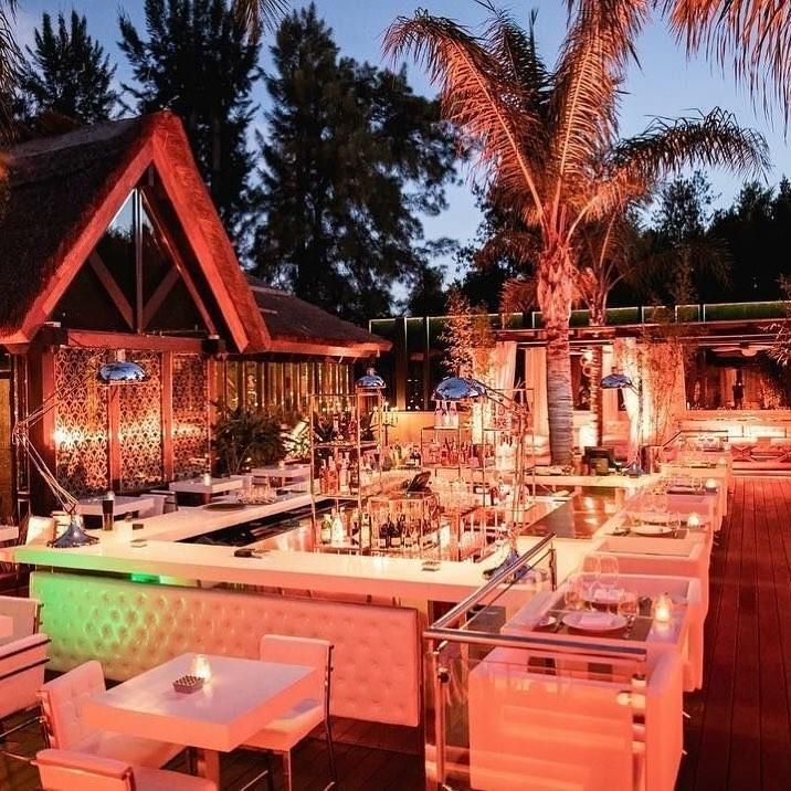 Bar al aire libre al anochecer con muebles blancos, barra e iluminación suave.